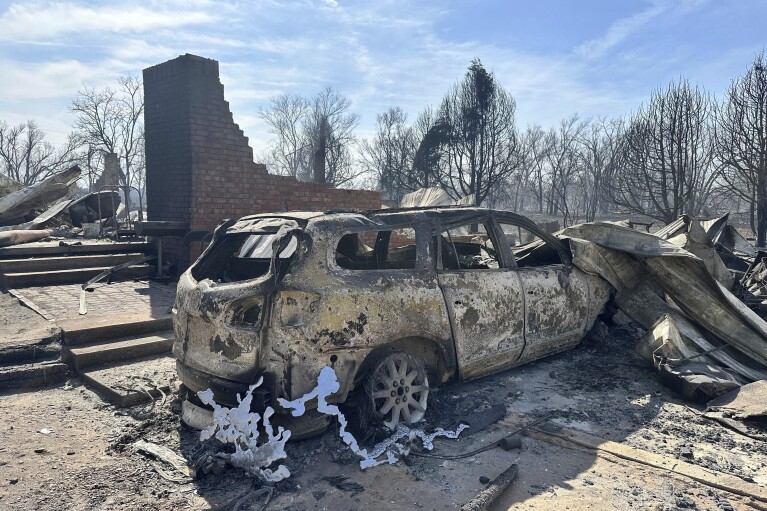 A burned car rests near the charred remains of a home outside of Canadian, Texas, Wednesday, Feb. 28, 2024, after a wildfire passed. A fast-moving wildfire burning through the Texas Panhandle grew into the second-largest blaze in state history Wednesday, forcing evacuations and triggering power outages as firefighters struggled to contain the widening flames. (AP Photo/Sean Murphy)